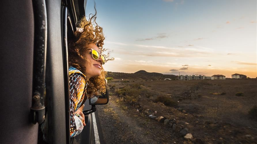 Woman with curly hair  blowing in the wind while she gazes at the sky from the car window. 