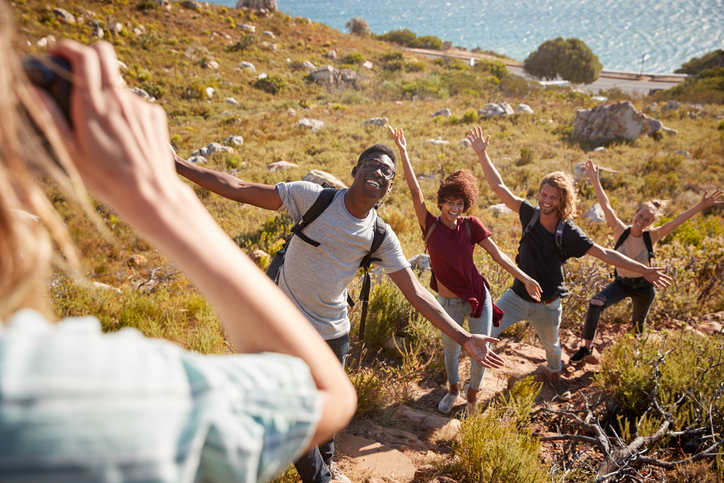 A group of young adults smiling posing with their arms up while on vacation. 