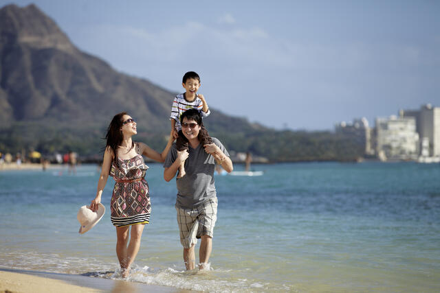 Family of three walking along the beach in Hawaii on a family beach vacation. 