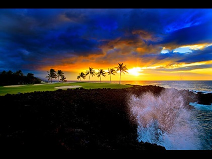 Waves crashing against palm tree line cliff at sunset a Ocean Tower by Hilton Grand Vacations Big Island resort in Hawaii. 