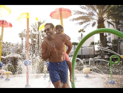 Dad and son smiling and playing in the splash pad at Las Palmaras by Hilton Grand Vacations in Orlando, Florida. 