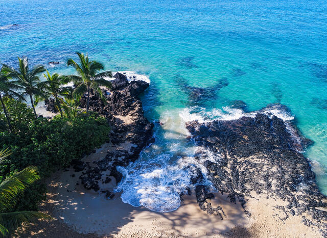Aerial shot of turquois waves crashing against black rocks on Maui in Hawaii. 