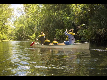 Family canoeing down a Florida tree-lined waterway. 