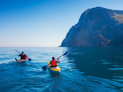 Two people paddling in the Pacific ocean with Hawaii's mountians in the distance. 