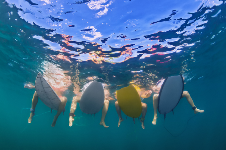 Under water shot of a group of female surfers' feet while they sit on surfboards.