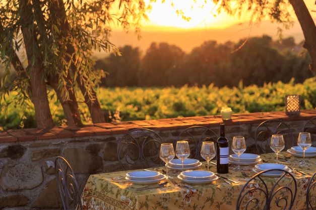 An outdoor dining table set near a vineyard at sunset in Tuscany, Italy