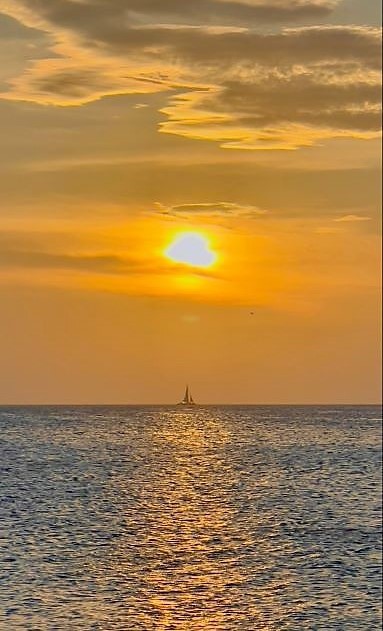 Beautiful image of sail boat on horizon and sinking sun overhead, Aruba. 