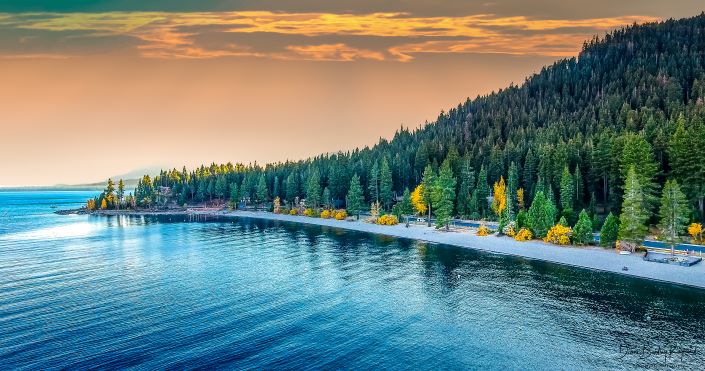 Beautiful aerial image of Lake Tahoe, fall folliage and blue waters with orange sunset skies overhead, Nevada. 
