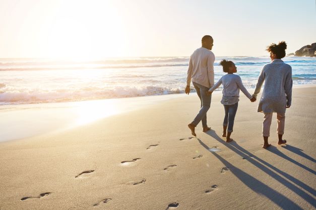 A family holding hands and walking barefoot on a beach at sunrise