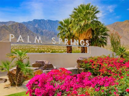 A sign that reads "Palm Springs" with palm trees and bougainvillea