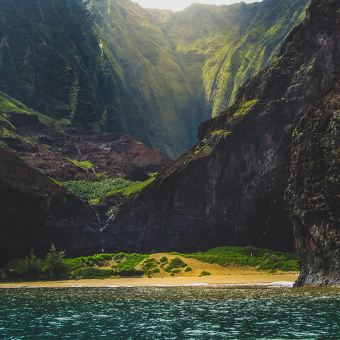 Sun shining through mountain lined beach in Hawaii. 