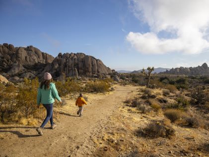 A parent and child in winter clothing walking along a desert trail near Palm Springs, California