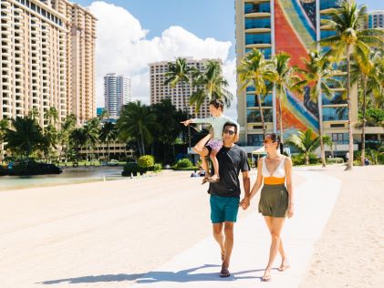 Two parents and their child walk along the sand of the lagoon at Hilton Hawaiian Village® in Honolulu, Hawaii