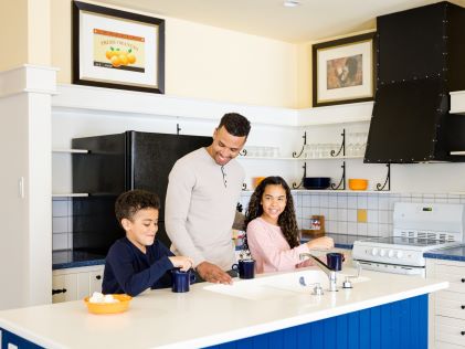 A dad and two kids prepare hot chocolate in the in-Suite kitchen of Tremblant, a Hilton Grand Vacations Club in Quebec, Canada
