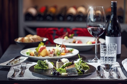 Table set for fine dining in Las Vegas including a glass of wine and colorful plates of appetizers with wine rack seen in the background. 