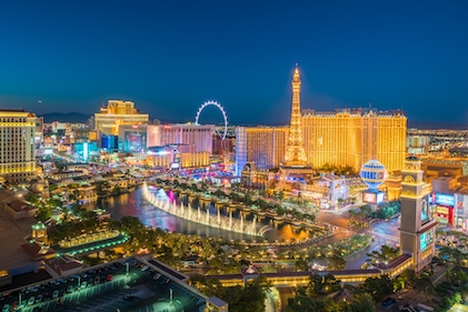 Long shot of the Las Vegas Strip just after dusk. Bright lights and attractions dot the skyline with a warm glow.
