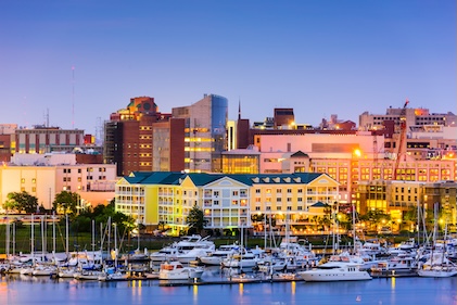 View of power boats lining the Charleston, SC harbor and the buildings beyond. Blue water is in the foreground and blue skies are overhead.