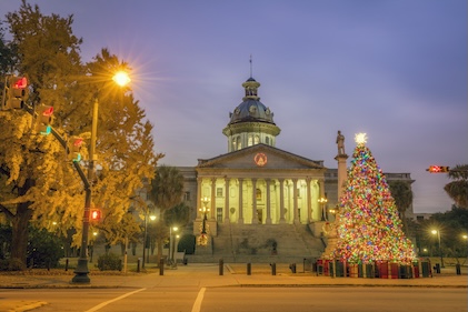 Winter scene with Christmas tree and lights in the foreground in front of the white and warmly-lit Charleston, SC state house.
