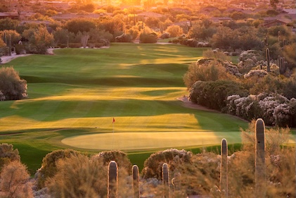 Golden rays of the sun fall across an Arizona golf course and its surrounding trees and cacti.