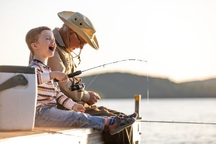 Mature male happily fishing with young boy. 