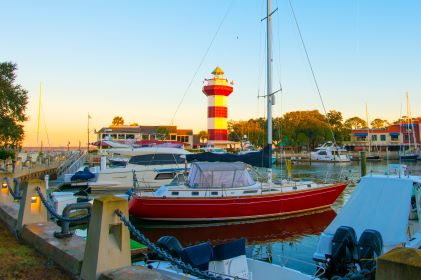 Boat-filled marina at sunset, sun shining on Harbour Town Lighthouse, golden hour, Hilton Head, South Carolina. 