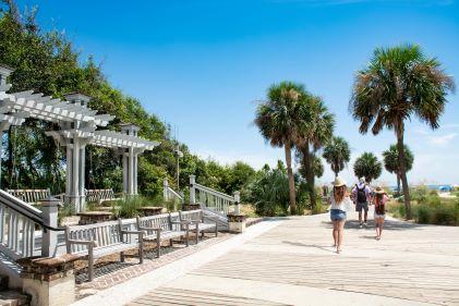 Group of people walking along water's edge, manicured walkway line with palm trees, Hilton Head, South Carolina. 