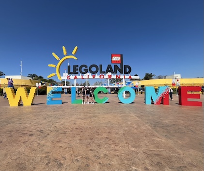 Long shot of very colorful Welcome entrance sign to Legoland(R) California with three young women standing in front of the sign, in the distance.