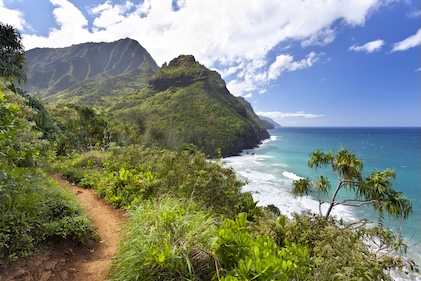 Image of shoreline and volcanic mountains with a copper-colored path running parallel to the shoreline toward the mountains. Path is surrounded by lush vegetation.