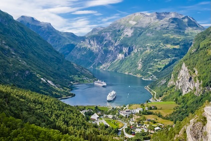 Aerial view of Norway Fjords surrounding a body of water with cruise ships. The fjords are tall and green against a blue sky.