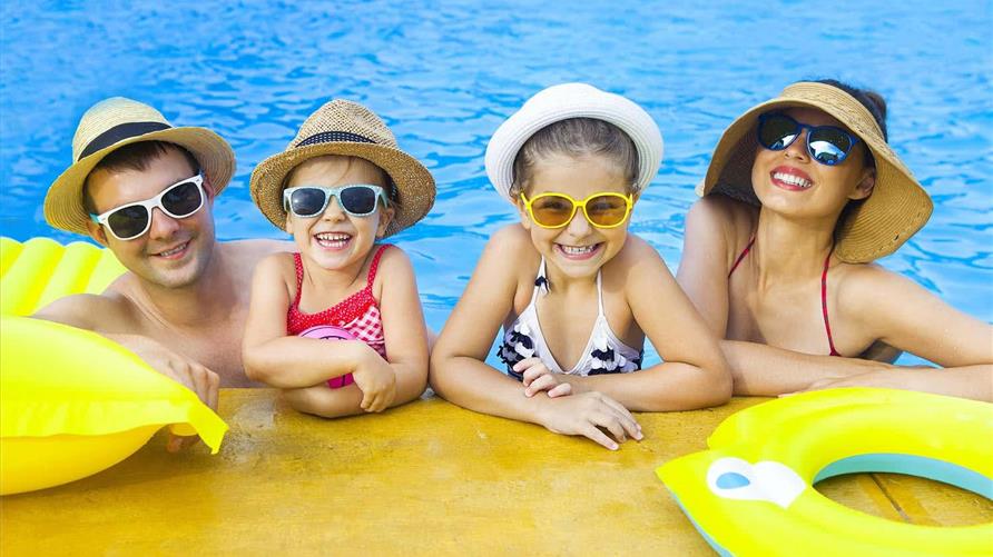A happy family on a family vacation smiling in the pool wearing hats and sunglasses. 