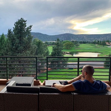 A man surveys the Ridge on Sedona golf course backdropped by the Arizona mountains while seated on a couch on a balcony.