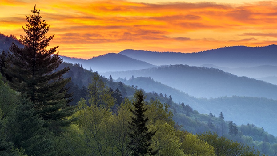 The sun rises in an orange sky about the foggy Smoky mountains